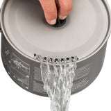 A hand holds a pot lid while water pours out through a series of small holes on the side of the Sea to Summit Alpha Cookset 4.2, made from high-spec anodised alloy and perfect for any durable, lightweight camp kitchen set.
