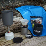 The Soto Navigator Camping Cookware Set by Soto, featuring a portable stove, pot, collapsible coffee dripper, fuel canister, and versatile cookware, is ideal for outdoor cooking gear enthusiasts—compact and ready next to your blue mat.