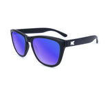 Knockaround Premium Sunglasses boast black frames with blue mirrored, impact-resistant lenses offering UV400 protection. Adorned with a white "K" logo on the temples, these polarized sunglasses by Knockaround combine style and functionality.