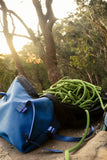 A Blue Tag Equipment Magic Carpet Rope Bag rests outdoors on dirt, surrounded by trees and sunlight—essential gear from Blue Tag Equipment for your next Grampians climbing adventure.