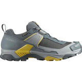 The Salomon X Ultra 5 Men's Hiking Shoe features a rugged Contagrip sole, mesh/synthetic materials, Gore-Tex for weather protection, a heel pull tab, visible Salomon branding, and StabilityAdvanced Chassis for enhanced support in grey and yellow.