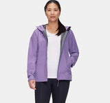 A woman stands facing forward, one hand in her pocket, wearing a Mammut Alto Light HS Women's Jacket in light purple over a white shirt and black pants.