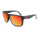 The Knockaround Torrey Pines Sunglasses from Knockaround feature black frames with rectangular, orange-tinted lenses that offer UV400 protection, and a small red "K" logo on the temple.