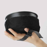 A hand holds the Soto Navigator Camping Cookware Set by Soto, featuring a round metal container in a black mesh sleeve with gray adjustable strap—ideal for your camping cookware set or outdoor cooking gear.