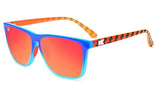 A pair of Knockaround Fast Lane Sport Sunglasses with blue frames and orange gradient, polarized lenses for optimal clarity. The temples are orange with a wavy black pattern and contain a white "K" logo, offering stylish UV protection.
