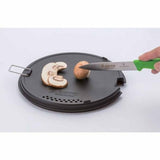 A hand uses a knife to slice a mushroom on the round black cutting board from the Soto Navigator Camping Cookware Set—ideal gear for outdoor cooking enthusiasts by Soto.