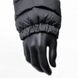 A close-up of a matte black mannequin hand wearing a 3 Peaks Women's Down Jacket with an elastic cuff, showcasing its durable water repellent fabric and high warmth to weight ratio, against a white background.