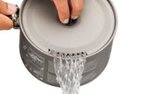 A hand holds the lid of a Sea to Summit Alpha Cook Set 2.1 pot with water pouring out through small holes along the edge, against a white background.