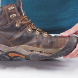 A person holding a worn, brown hiking boot with a detached sole considers using Gear Aid Aquaseal Shoe Repair Glue for a reliable fix.
