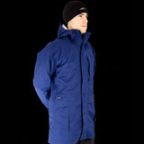 A person wearing a blue hooded Mont Men's Austral JKT made of Hydronaute fabric and a black beanie stands against a black background, looking to the side.