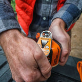 Person using a Jetboil Crunchit fuel recycling tool on an orange butane fuel canister, wearing a plaid shirt and red vest.