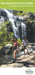 Two hikers at Grampians National Park; one woman posing by a rocky stream and a waterfall, another man walking behind her on the Parks Victoria Wonderland/Central Day Walks Map trail, surrounded by lush greenery.