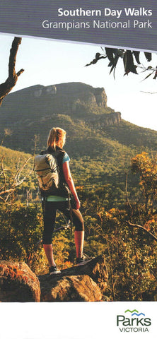 A woman stands on a rock, looking out at the Grampians National Park, with dense forests and a large mountain in the background, using the Parks Victoria Southern Day Walks Map.