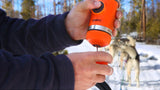 With hands wrapped around a Wacaco Nanopresso, its vibrant orange color stands out against the snowy landscape as it dispenses rich coffee outdoors. Surrounded by sled dogs and the crisp winter air, this portable espresso maker from Wacaco provides the perfect brew amidst nature's vast beauty.