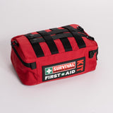 A red first aid kit bag labeled "Survival First Aid" and "Survival Workplace First Aid Kit," featuring black straps, a zippered closure, and designed with a water-resistant exterior.