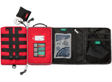 A Survival First Aid, compact Survival Workplace First Aid Kit with multiple compartments, featuring a MOLLE system for easy attachment. It includes various medical supplies like a roll of tape, scissors, bandages, an instant ice pack, and labeled pouches for organized storage.