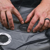 A person uses both hands to apply a Gear Aid Tenacious Tape Mesh Patch 75mm to a tear in black fabric, drawing from their trusty camping repair kit.