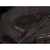 Close-up of a black jacket made with Gear Aid's Gore-Tex Fabric Patches, featuring a patch on the sleeve and a zippered pocket. This durable Gear Aid jacket showcases its Gore-Tex Fabric Patches, ideal for reinforcement and style.