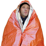 A person in a black hat and jacket is wrapped in an orange and silver SOL Emergency Blanket from SOL, made of vacuum-metalized polyethylene.
