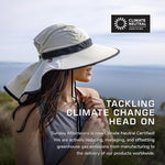 A person wearing the Sunday Afternoons Shade Goddess, which features a "Climate Neutral Certified" badge, gazes at the water. The text reads, "Tackling Climate Change Head On," emphasizing sun protection and lightweight fabrics in climate certification efforts by Sunday Afternoons.