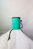 A teal cylindrical pouch with a drawstring toggle and a black cord, displayed against a plain white background. The Blue Tag Equipment Chalk Bag by Blue Tag Equipment combines practicality with style, featuring a cozy fleece lining.