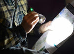 A person examines a map with a UCO Pika 3-in-1 Rechargeable Lantern in a dimly lit environment, focusing on a specific area illuminated by the light.