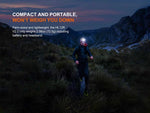 At dusk, a person runs through grassy mountains wearing the Fenix Lighting HL12R V2.0 SST20 white & 2835 Red LED headlamp. Text highlights its compact, lightweight design and 500 lumen power—ideal for outdoor adventures from Fenix Lighting.
