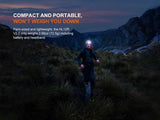 At dusk, a person runs through grassy mountains wearing the Fenix Lighting HL12R V2.0 SST20 white & 2835 Red LED headlamp. Text highlights its compact, lightweight design and 500 lumen power—ideal for outdoor adventures from Fenix Lighting.