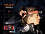 A woman adjusts the Fenix Lighting HM65R-T V2.0 headlamp with a side dial amid dusk trees; text highlights its adjustable headband and hands-free lighting featuring Luminus SST40 & OSRAM GW PUSTA1.PM LEDs.