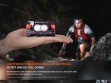 A person holds the Fenix Lighting HM65R-T V2.0 headlamp with Luminus SST40 & OSRAM LEDs, while a runner in outdoor gear is blurred in the background. Text highlights its lightweight magnesium alloy for hands-free adventure lighting.