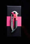 *Koi Knives'* "Garry" | The Galah EDC Pocket Knife, featuring a red handle and partially serrated blade, ideal for camping adventures, is elegantly displayed on a black rectangular box with a pink band.