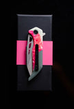 *Koi Knives'* "Garry" | The Galah EDC Pocket Knife, featuring a red handle and partially serrated blade, ideal for camping adventures, is elegantly displayed on a black rectangular box with a pink band.