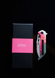 A folding pocket knife, named the Koi "Garry" with a pink and black handle, is placed next to a sleek black box, making it ideal for camping adventures. The box features a pink label with the text "The Galah" from Koi Knives South Australia.