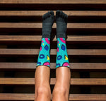 A woman's legs with Injinji Spectrum Trail Women's Midweight Crew socks rest on a wooden bench.