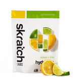 A package of Skratch Labs Sport Hydration Drink Mix 440g in lemon and lime flavor is displayed upright, highlighting its low sugar content and vital electrolytes, accompanied by a sliced orange and lime.