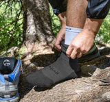 A man is putting on a pair of Injinji Outdoor Hiker & Liner Men's Crew socks from a sock set.