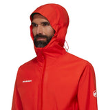 A man in a bright red Mammut Alto Light HS Men's waterproof hiking jacket with the hood up, showing the Mammut logo on the chest and sleeve.