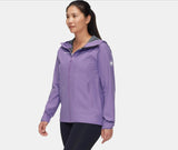 A woman wearing the Mammut Alto Light HS Women's Jacket in light purple with a hood and black leggings walks forward against a plain light background.