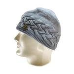 The Domex Beanie by Domex is a light gray knit hat featuring a braided pattern and round metallic logo on the side, shown on a white mannequin head—ideal for anyone wanting a warm, stylish winter beanie.