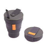 The Hunu Collapsible Cup by Hunu is a gray silicone travel cup with a BPA-free sleeve and orange tag, shown with its leak-proof lid and straw beside the cup.