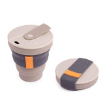 Two Hunu Collapsible Cups by Hunu, both BPA-free with lids: one expanded, one folded flat. Each features a grey band with orange tab and a leak-proof design for worry-free travel.