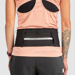 Person wearing a peach tank top and an Ultimate Direction Utility Belt in black, standing with back to the camera and showing a left arm tattoo. The no-bounce design of the Utility Belt offers comfortable movement.