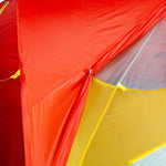 Close-up of the Mont Moondance EX Tent by Mont, a brightly colored ultralight backpacking tent featuring red, yellow, and orange sections. The image emphasizes the stitching and reinforced seams made from durable materials.