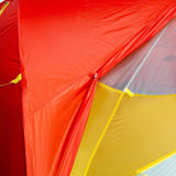 Close-up of the Mont Moondance EX Tent by Mont, a brightly colored ultralight backpacking tent featuring red, yellow, and orange sections. The image emphasizes the stitching and reinforced seams made from durable materials.