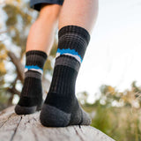 Close-up of a person wearing Wilderness Wear Grampians Peak Merino eXtreme Hiker Socks made from merino wool, standing outdoors on a wooden plank with blurred trees and sky in the background.