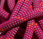 Close-up of intertwined, vibrant Mammut 9.5 Crag Dry Ropes featuring a woven pattern with pink, orange, grey, and red threads.